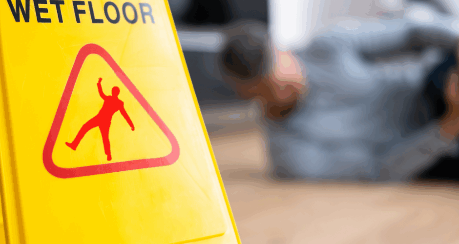 Wet Floor hazard sign with a man on ground behind