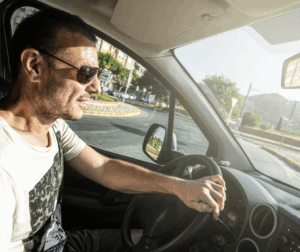 A man driving his car wearing sunglasses and the sun glaring into his car