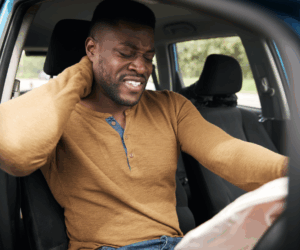 A man in the driver seat holding his neck after an accident