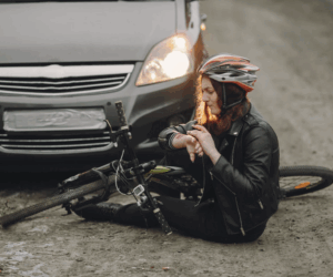 Woman in bicycle helmet with bike on road infront of a car