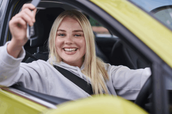 Happy teenage girl holding car keys behind the wheel